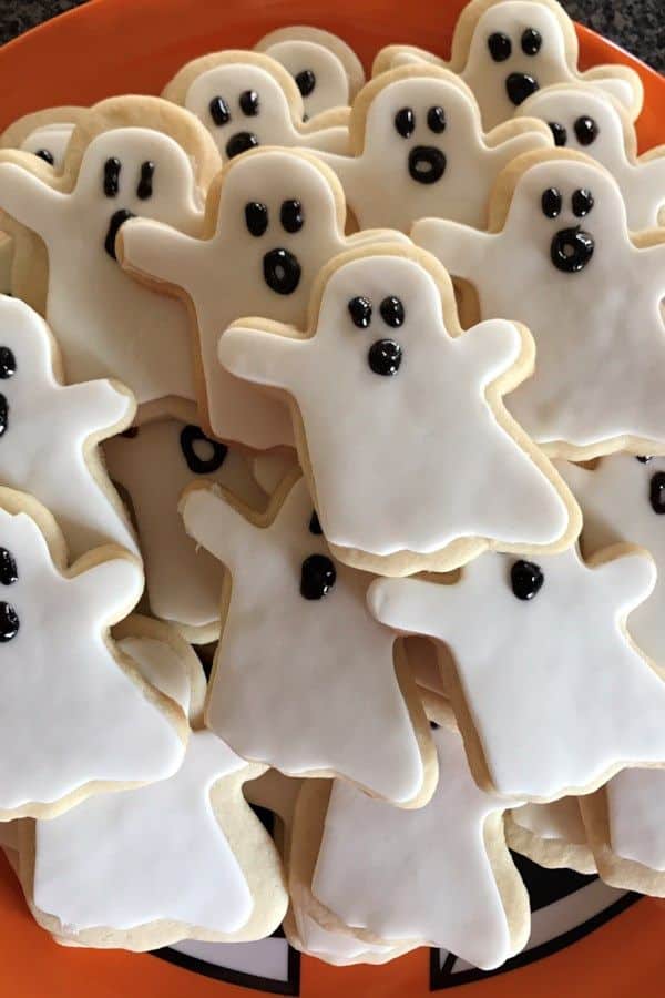 A plate of ghost-shaped Halloween cookies decorated with white icing and black eyes and mouths, perfect for a festive treat.