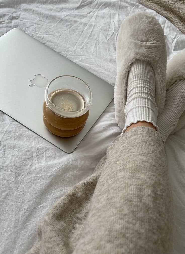 Cozy morning with coffee, fuzzy slippers, and laptop on bed, creating a relaxing work-from-home vibe.