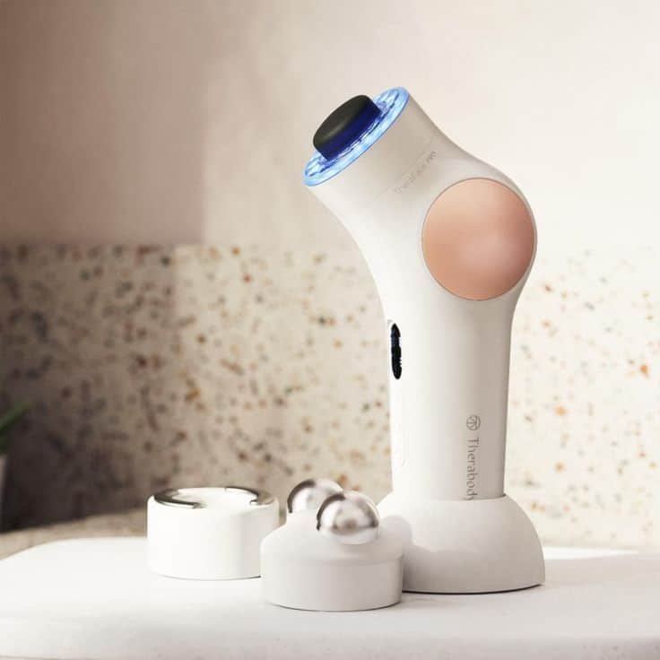 Handheld skincare device with LED technology on marble surface, featuring interchangeable heads for facial treatments.