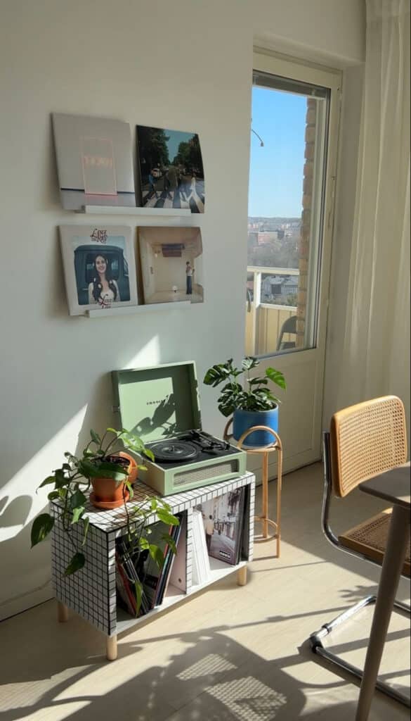 Modern living room with vinyl records, green turntable, plants, wall art, and natural light through a window. Cozy and stylish decor.