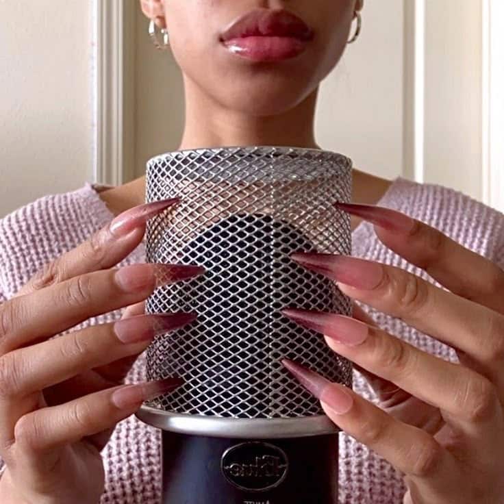 Person with long nails holding a microphone, ready for ASMR or podcast recording.
