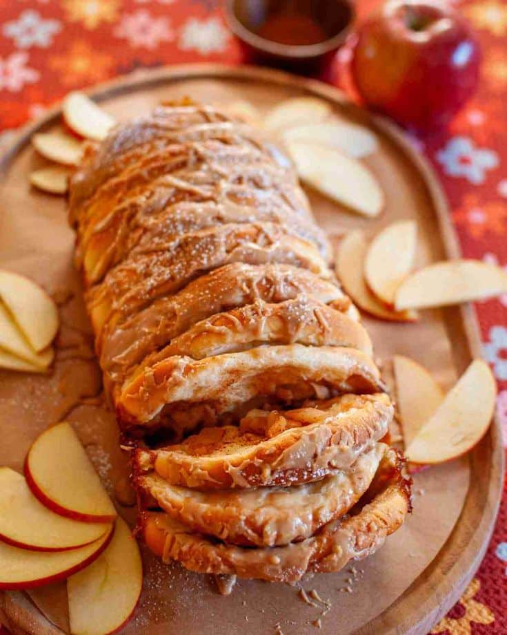 Delicious apple strudel with icing and sliced apples on a wooden tray, perfect for a cozy autumn dessert.