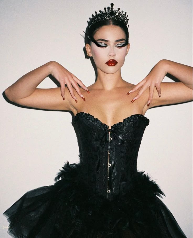 Elegant woman in a black corset and crown, dramatic makeup with bold eyeliner and red lips, striking a powerful pose.