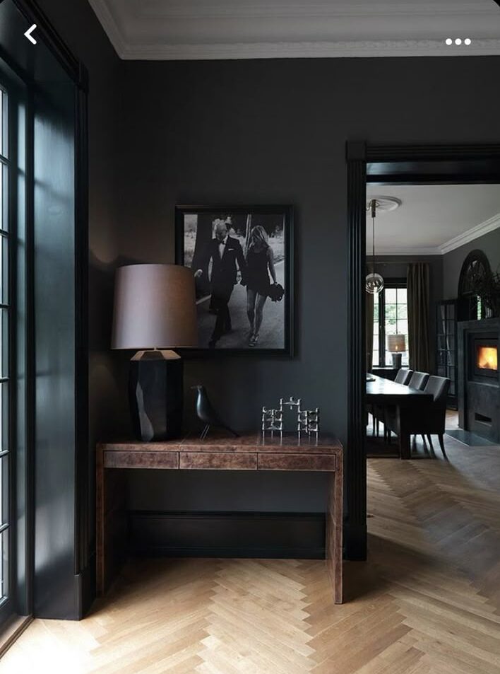 Elegant modern hallway with dark walls, wooden floors, and stylish decor including a desk, lamp, and black-and-white artwork.