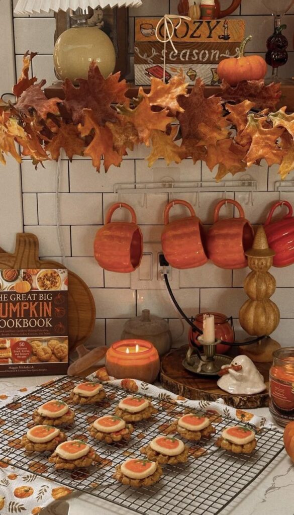 Cozy autumn kitchen with pumpkin cookies, cookbook, candles, and fall leaves, creating a warm seasonal atmosphere.