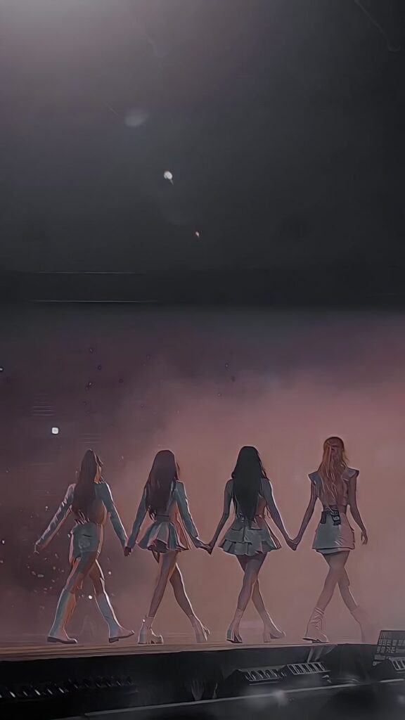 Four performers hold hands on stage in a captivating concert moment, illuminated by dramatic stage lighting.