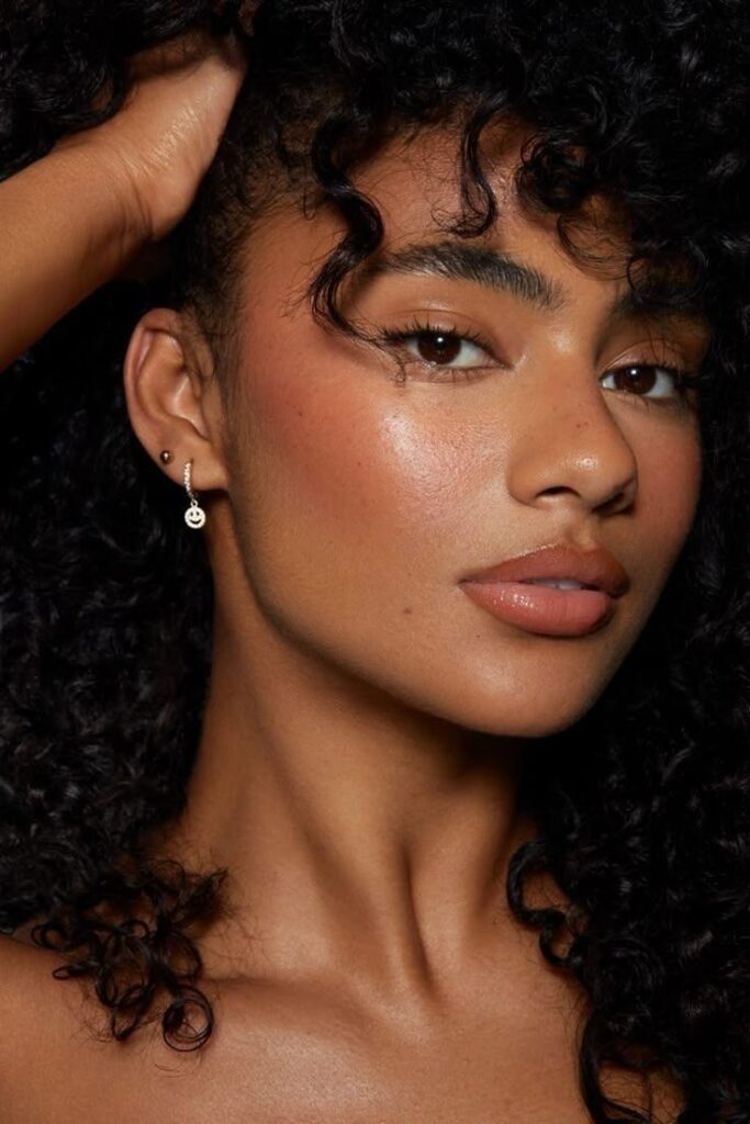 Curly-haired woman with radiant skin and elegant earrings, showcasing natural beauty and confidence.