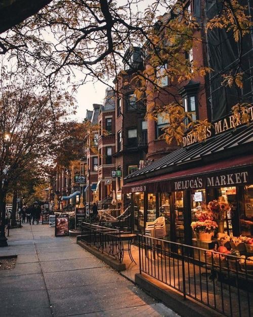 Quaint city street in autumn with a market, cozy lighting, and brownstone buildings, capturing a charming urban evening scene.