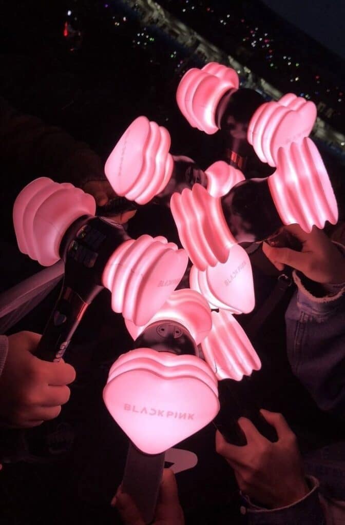 Fans holding glowing pink heart-shaped light sticks at a concert, creating a vibrant and energetic atmosphere.