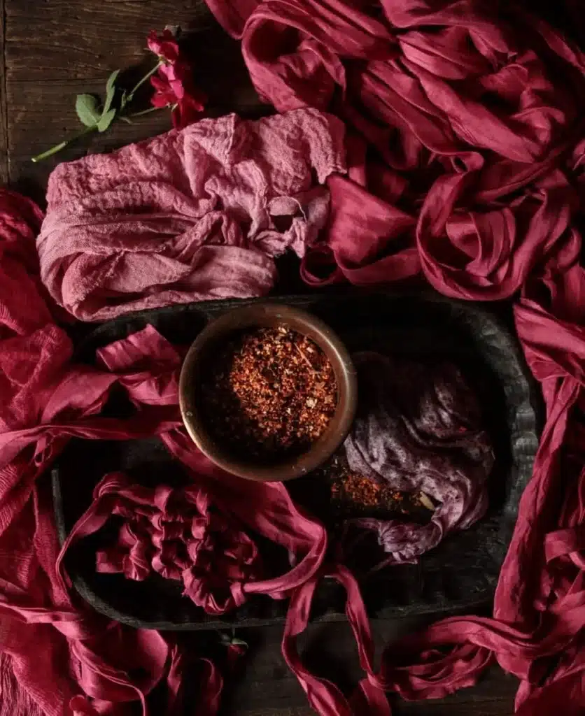 Assorted red and pink fabrics with a bowl of dried spices on a wooden table, enhancing rustic elegance and cozy aesthetics.
