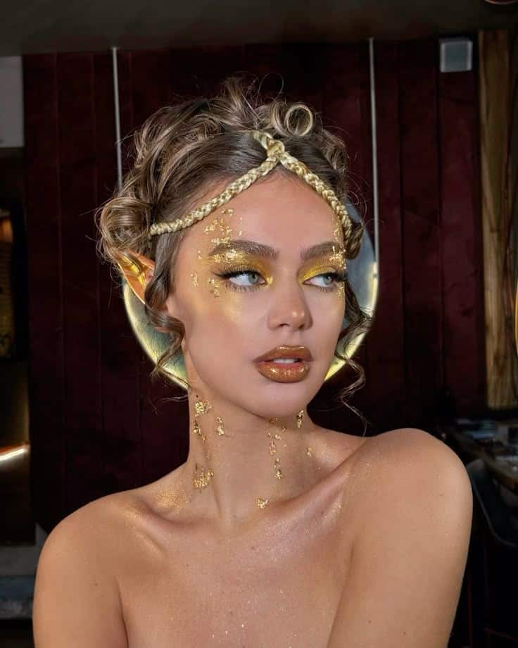 Woman with gold makeup and braided headpiece, glowing skin, fantasy-inspired look, bare shoulders, elegant and otherworldly atmosphere.