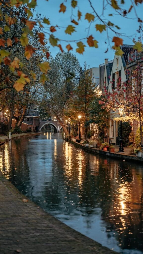 Charming canal scene at dusk with reflections, autumn leaves, and cozy buildings lining the water in a picturesque European town.