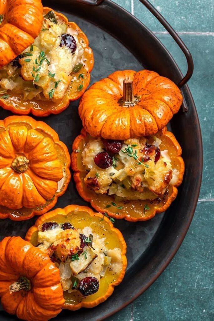 Stuffed mini pumpkins with savory filling featuring cranberries and herbs on a black tray, perfect for a festive fall dinner.