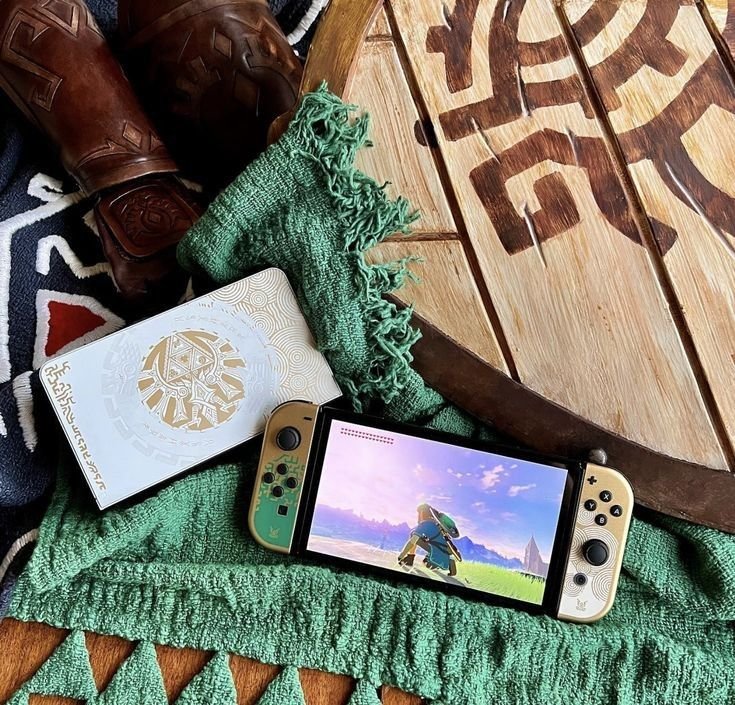 Nintendo Switch with Zelda-themed accessories and game on screen, alongside a decorative wooden shield and green cloth.