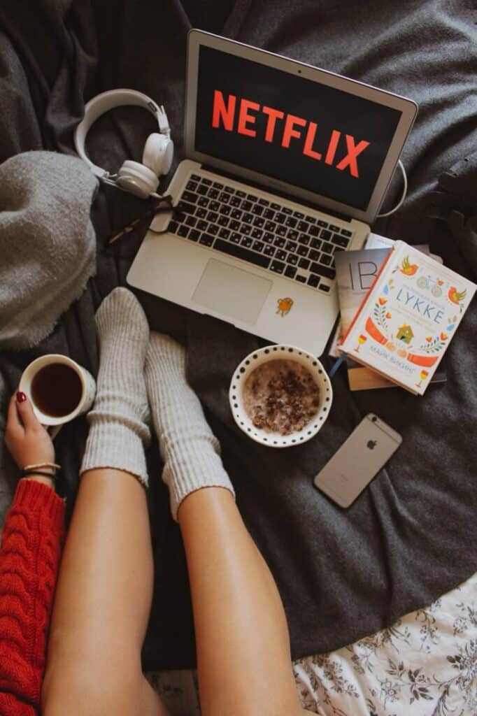 Cozy day in bed with Netflix, a book, oatmeal, and tea. Relaxation with warm socks and headphones. Perfect for a chill weekend.