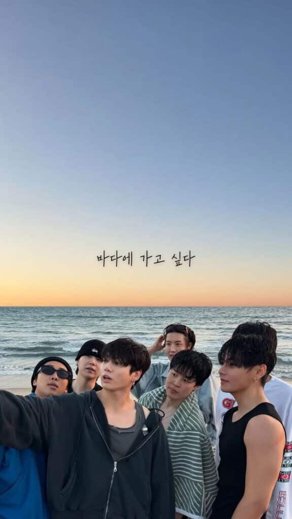 Group of friends taking a selfie on the beach at sunset with the ocean in the background.