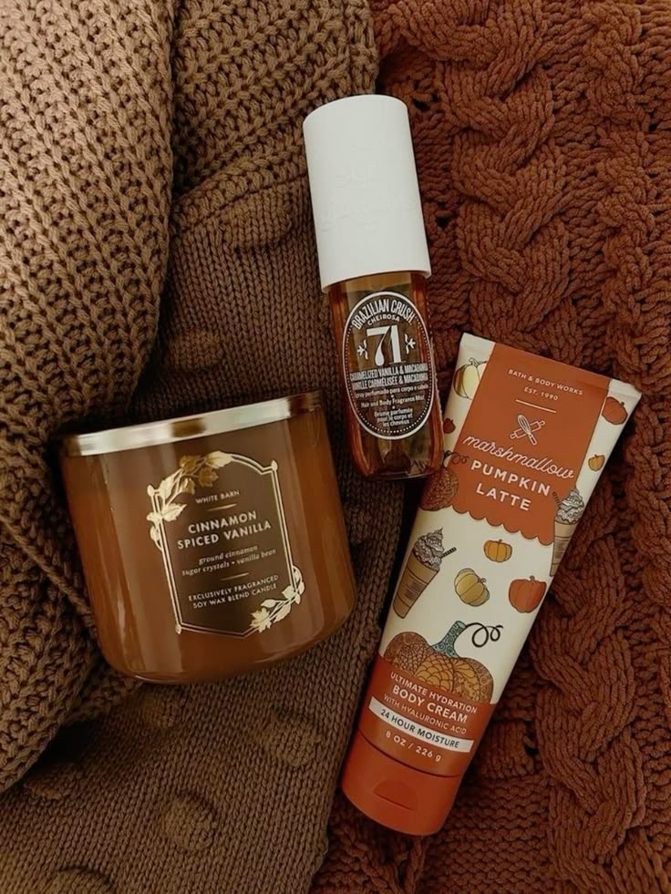 Cozy fall-themed products: cinnamon vanilla candle, Brazilian body mist, and pumpkin latte body cream on knitted brown fabric.