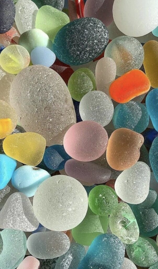 Colorful sea glass pebbles in various shapes and sizes, showcasing smooth textures and pastel hues in natural sunlight.