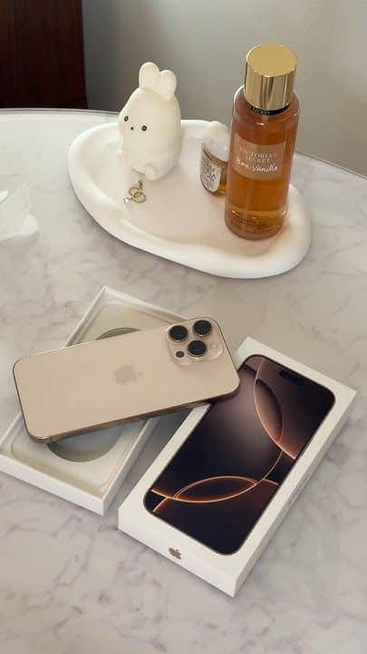 New smartphone with triple camera on marble table, next to fragrance bottle and cute ceramic figurine. Elegant tech display.