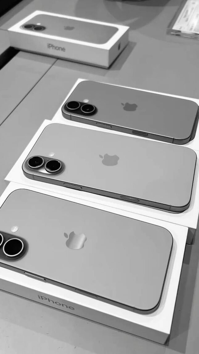 Three iPhones in boxes on a table, showcasing the sleek design and dual cameras, ready for unboxing.