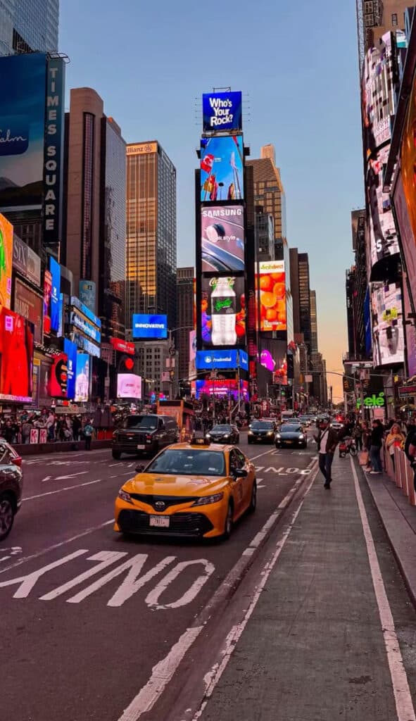 Times Square at dusk with vibrant billboards, traffic, and pedestrian activity, highlighting the iconic NYC atmosphere.