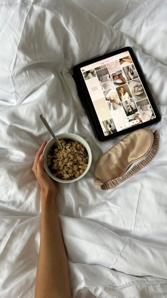 Cozy morning in bed with a healthy breakfast, tablet browsing, and a sleep mask on white sheets.