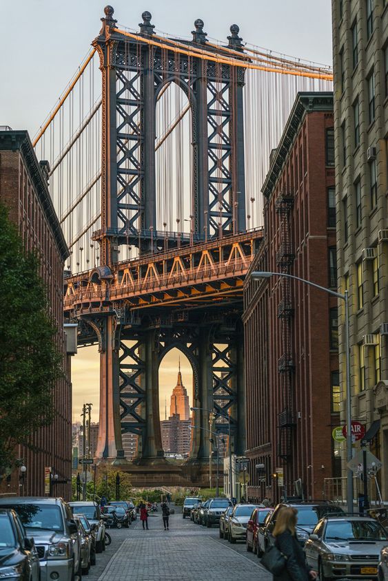 View of the Empire State Building framed by the Manhattan Bridge in Dumbo, Brooklyn, NYC, with surrounding buildings and street scene.