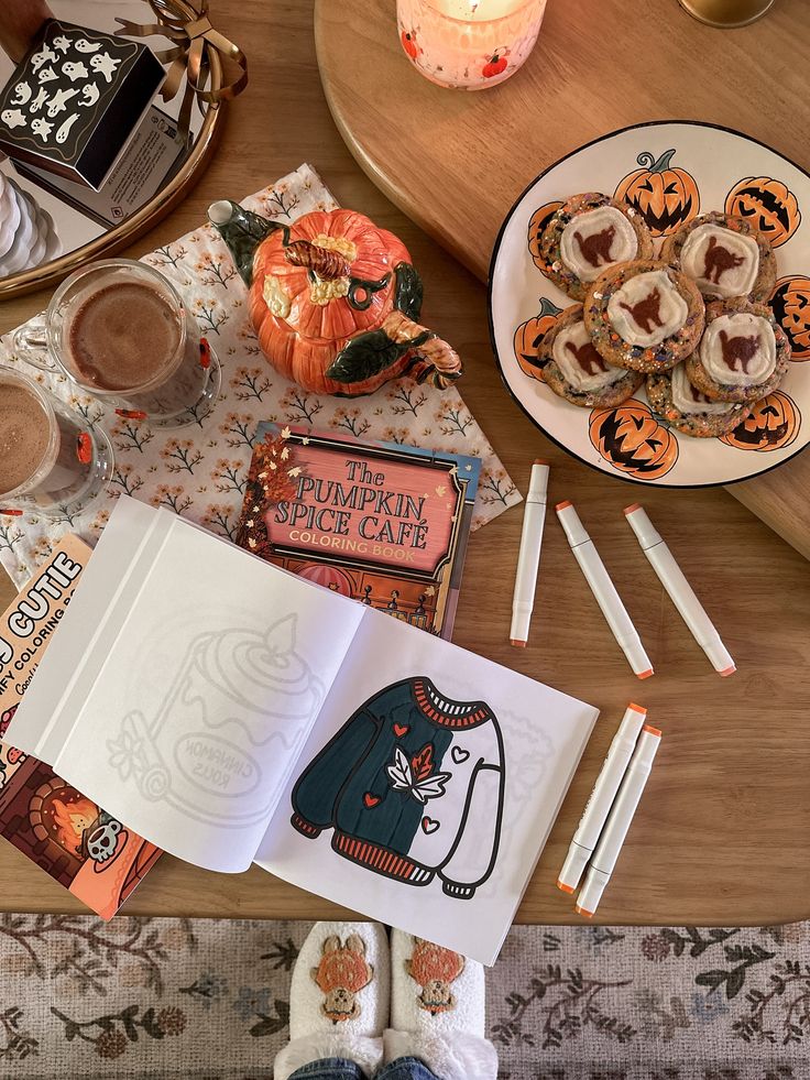 Cozy autumn setup with pumpkin spice drinks, cookies, a coloring book, markers, and festive decorations on a wooden table.