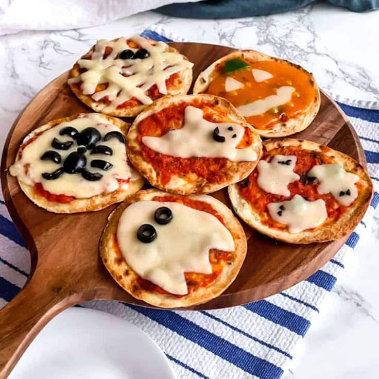 Mini Halloween-themed pizzas with ghost, pumpkin, and spider designs on a wooden platter, perfect for festive parties.