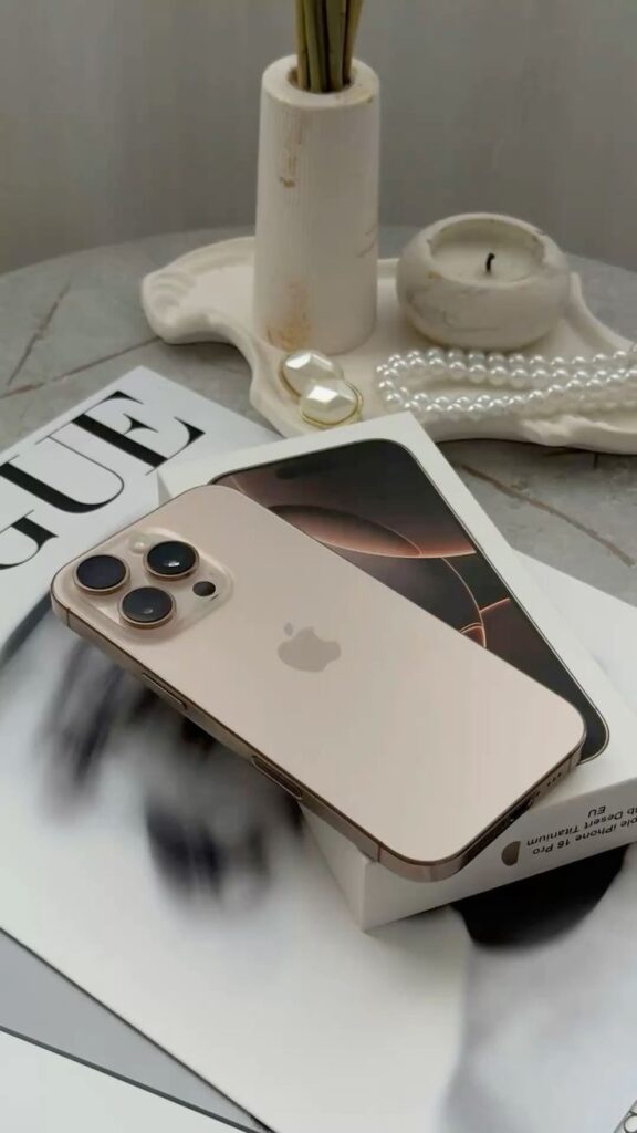 Gold smartphone on a magazine with pearl jewelry and candle, showcasing elegance and tech contrast.