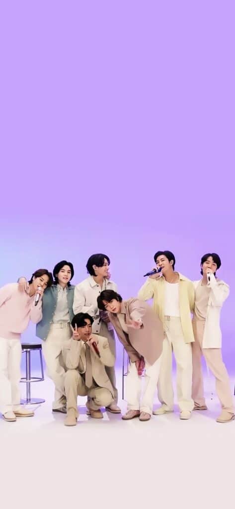 Group of seven young men in pastel outfits enjoying a lively moment together against a purple background.