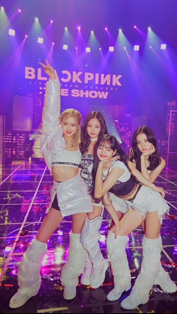 K-pop group performing on stage with vibrant lighting and stylish outfits during a live show.