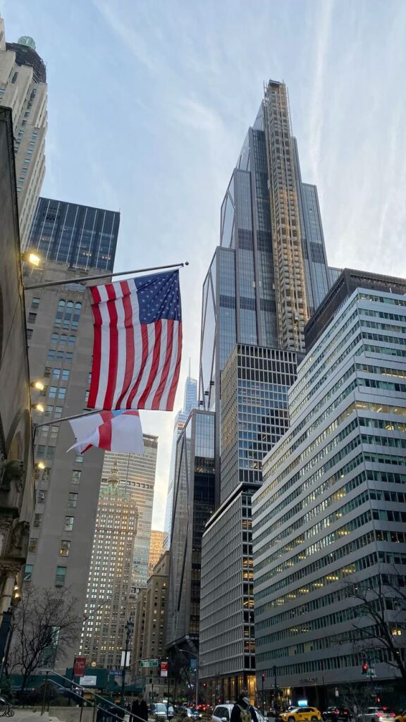 Tall skyscrapers and American flag in downtown cityscape with clear sky. Urban architecture and national pride.