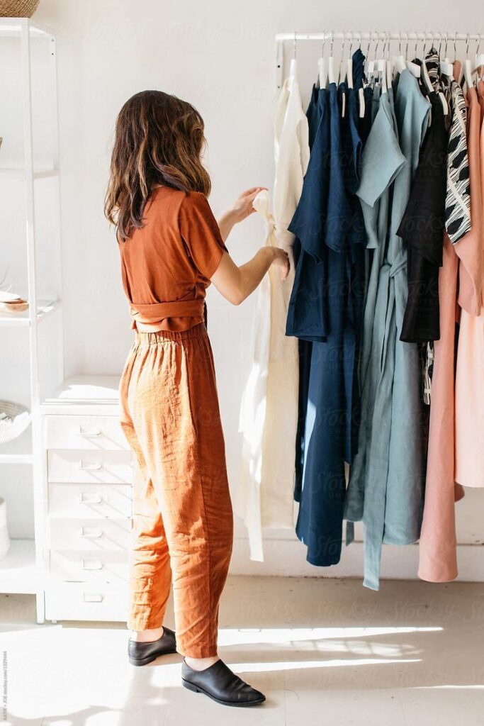 Woman in rust-colored outfit browsing dresses on a clothing rack in a bright, minimalist boutique. Fashion and shopping concept.