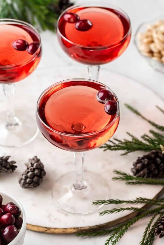 Festive cranberry cocktails in coupe glasses with fresh cranberries, perfect for holiday celebrations with pinecone and greenery decor.