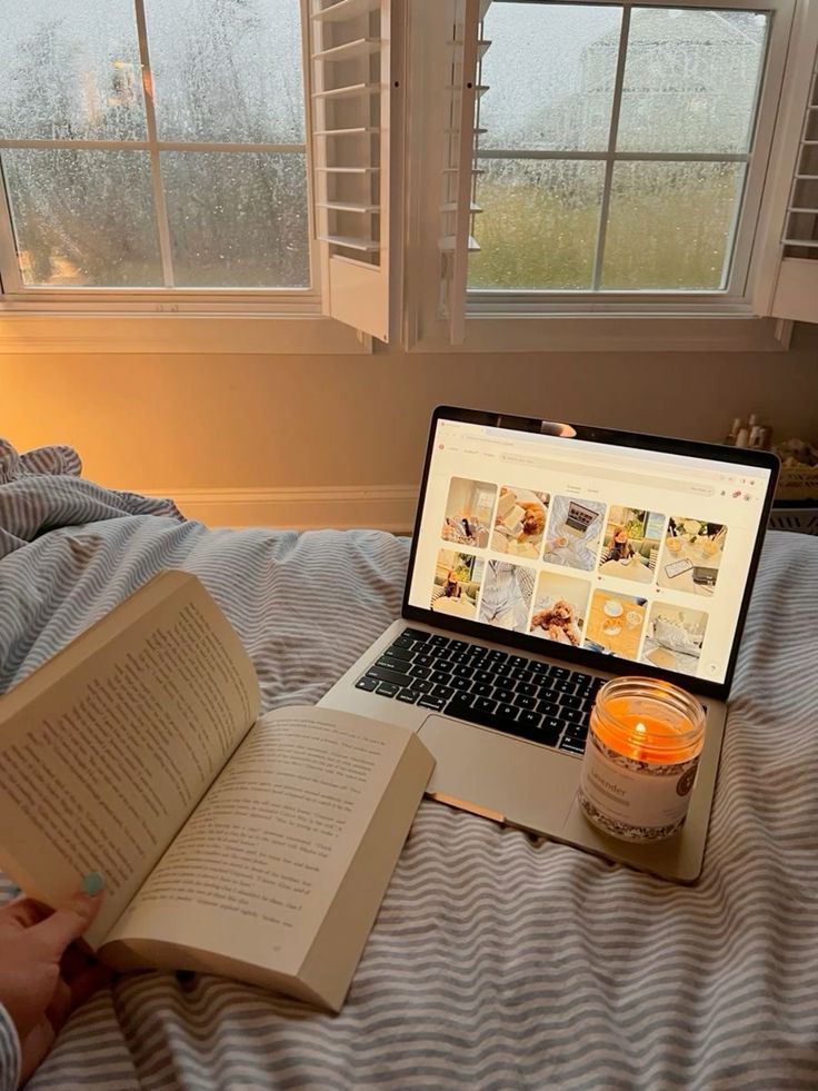 Cozy rainy day: Reading a book, browsing on a laptop, and enjoying a candle by the window. Perfect for relaxation and mindfulness.