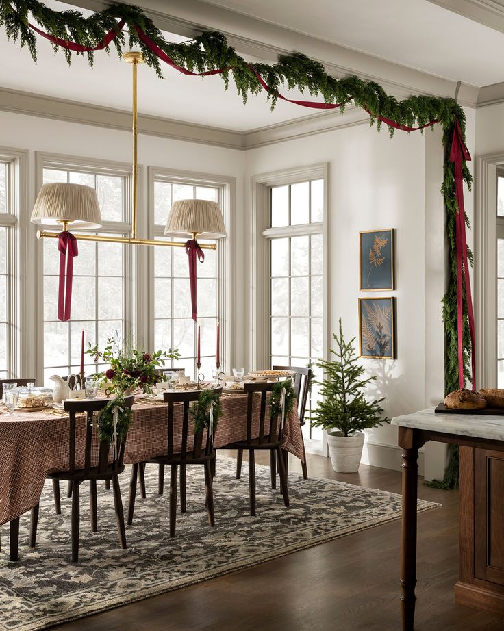 Elegant dining room decorated for Christmas with garlands, candles, and greenery, creating a cozy holiday atmosphere.