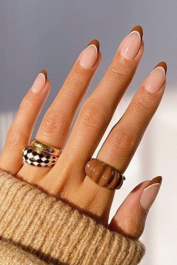 Stylish hand with geometric nail art and chunky rings, featuring nude and brown tones. Cozy vibe with a knitted sweater.