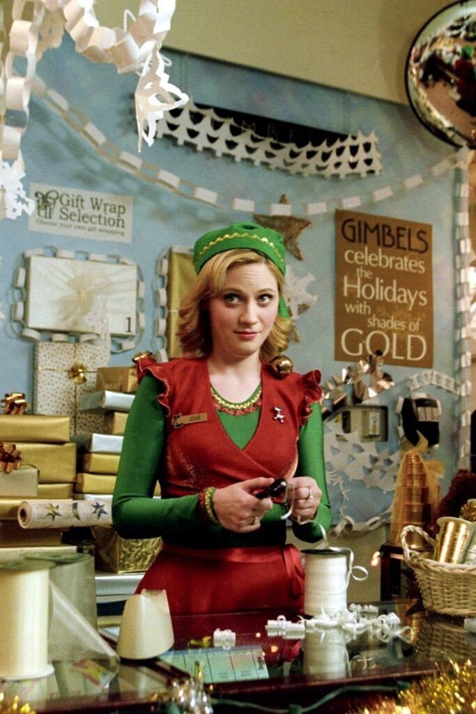 Gift shop employee in festive attire preparing holiday decorations at Gimbels store.