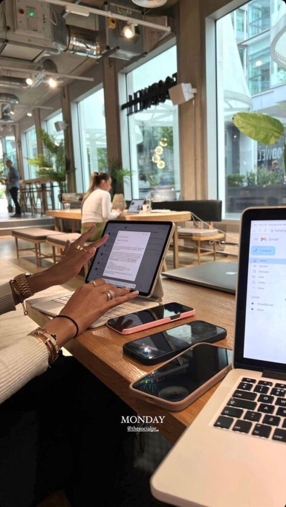 Woman working on a tablet in a modern cafe, surrounded by laptops and phones. Bright, productive workspace on Monday.