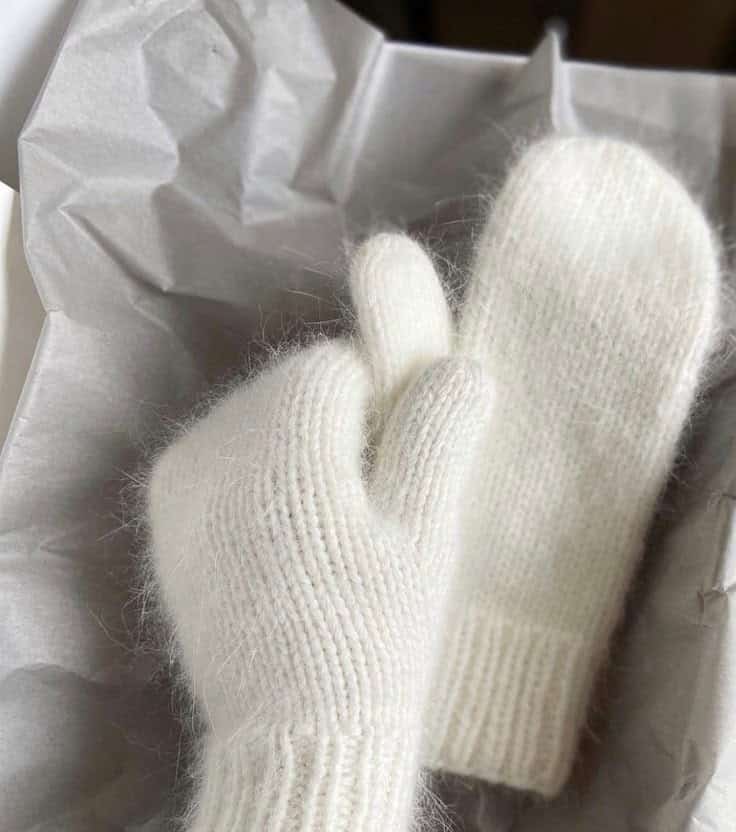 Cozy white knit mittens on crumpled tissue paper, perfect for keeping warm during winter. Soft and stylish handwear accessory.