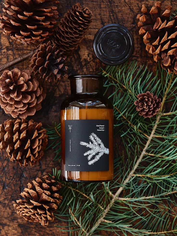 Balsam fir scented soy candle with pinecones and evergreen branches on rustic wood background for a cozy winter ambiance.