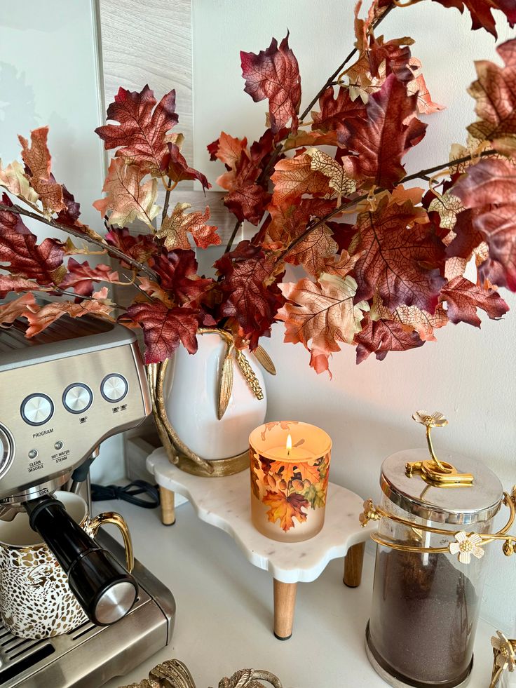 Autumn-themed decor with faux leaves, candle, and espresso machine on a cozy kitchen counter. Perfect for fall ambiance.
