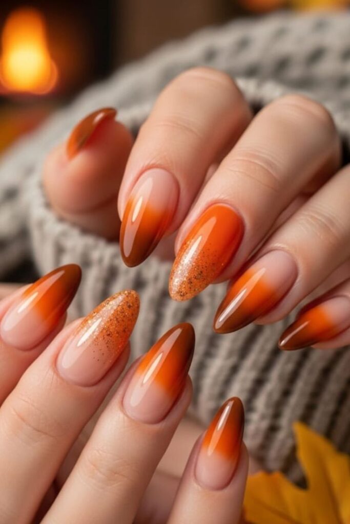 Autumn-themed nails with an orange ombre and glitter design, perfect for cozy fall vibes by the fireplace.