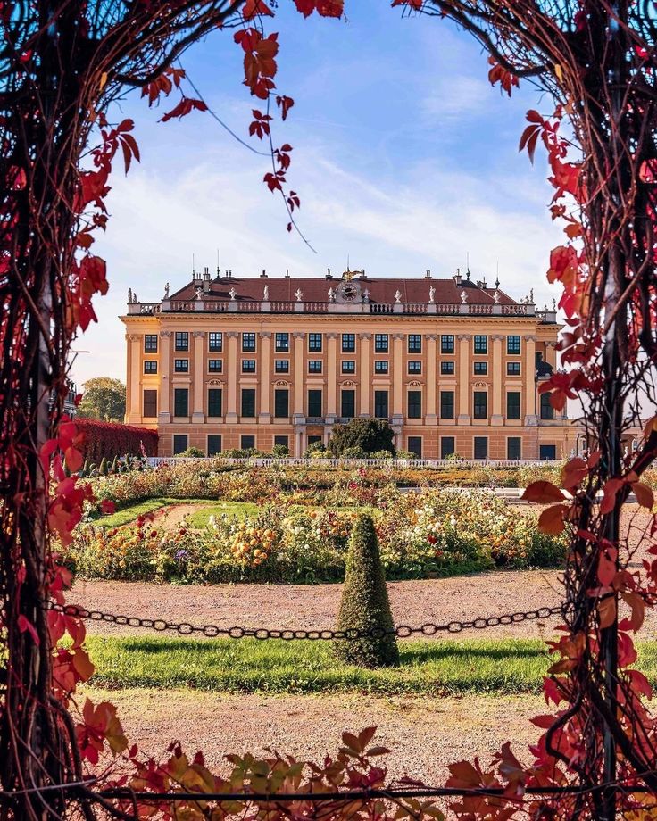 Elegant European palace framed by vibrant autumn foliage, showcasing a stunning garden landscape under a clear blue sky.