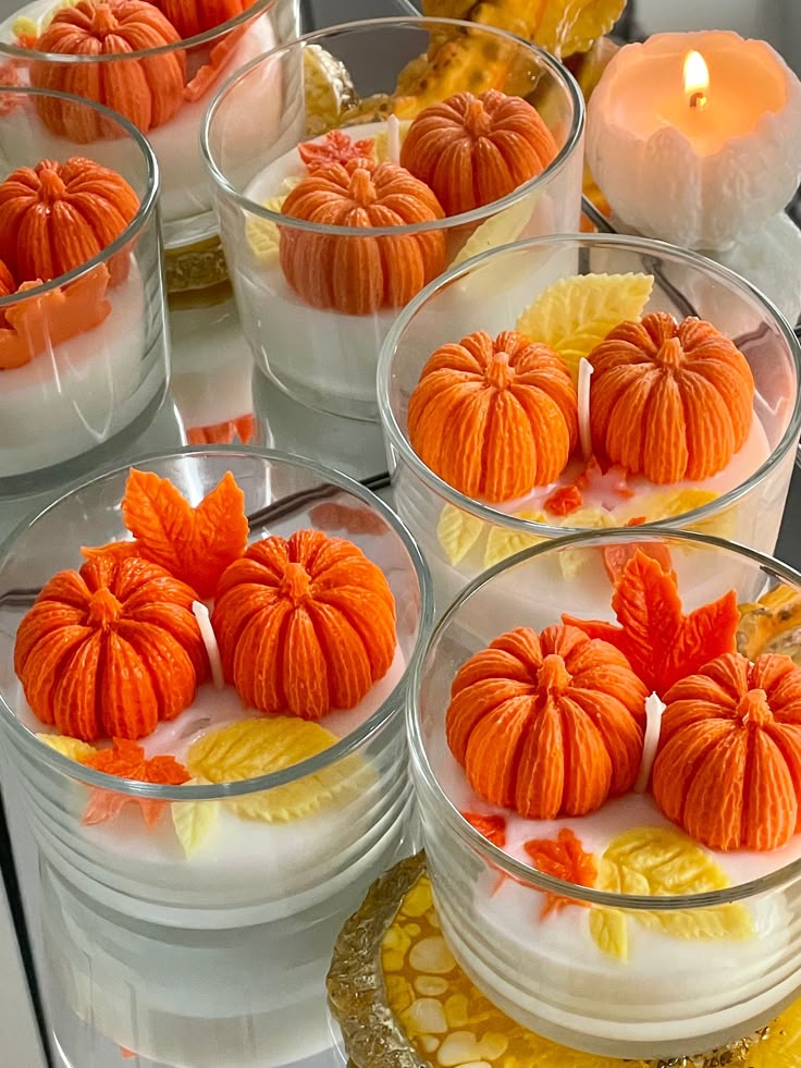 Decorative pumpkin candles in glass jars with autumn leaves, perfect for a cozy fall atmosphere.