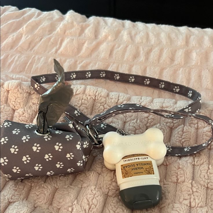 Dog leash with paw print design, attached waste bag dispenser, and bone-shaped hand sanitizer on a peach blanket.
