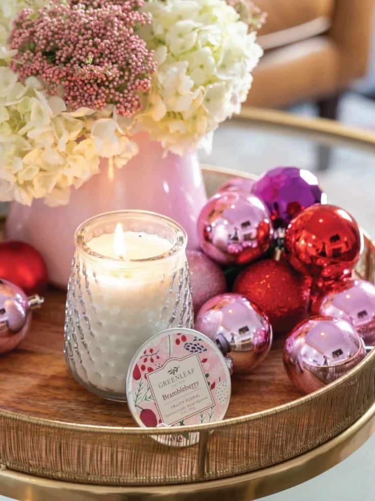 Elegant candle and festive ornaments on a gold tray with floral accents, creating a cozy, decorative ambiance.