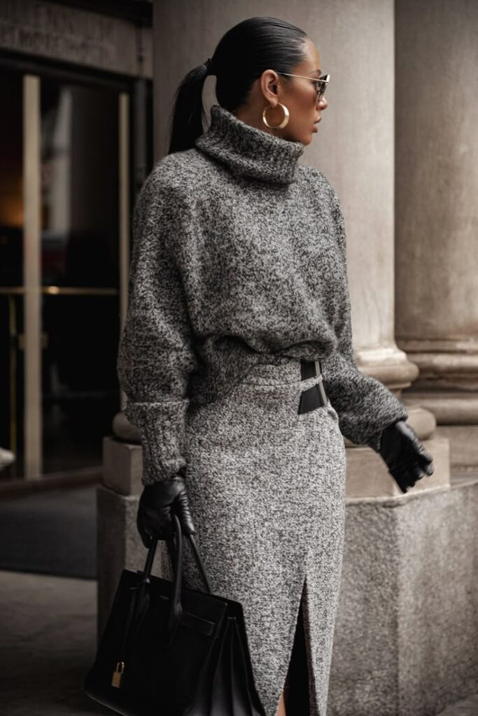 Stylish woman in grey turtleneck and skirt with black gloves and handbag, embracing chic urban fashion.