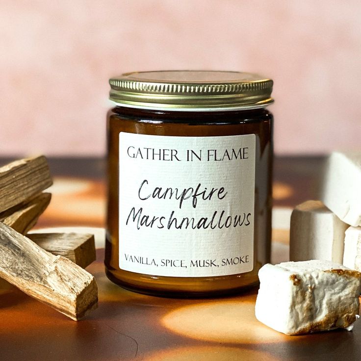 Jar candle labeled Campfire Marshmallows with wood and marshmallow accents, evoking vanilla, spice, musk, and smoke aroma.